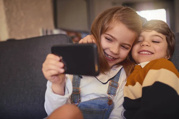 Sorridi. Ritagliato colpo di una bambina adorabile e il suo fratello minore scattare selfie mentre seduto sul divano a casa. — Foto Stock