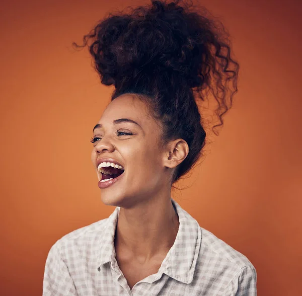 Não consigo parar de rir. Tiro de uma jovem mulher usando seu cabelo em um pão contra um fundo laranja. — Fotografia de Stock