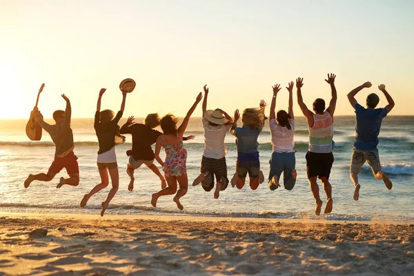 Dette er den beste sommeren noensinne. Bilder fra baksiden av en gruppe unge venner som hopper opp i luften på stranden. – stockfoto