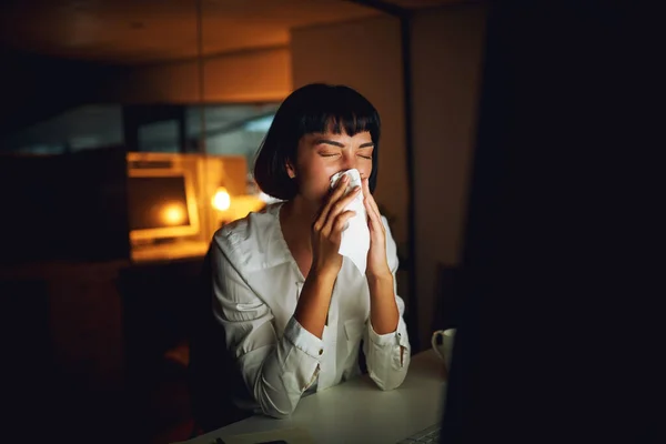 Teslim tarihi için sağlığını tehlikeye atıyor. Genç bir iş kadınının gece geç saatlerde işteyken burnunu silmesi.. — Stok fotoğraf