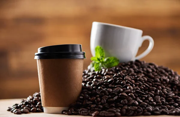 Una pequeña ramita de menta realmente aumenta el sabor. Primer plano de una taza de papel en una superficie, con una taza de té y una hoja de menta descansando sobre una pila de granos de café en el fondo. — Foto de Stock