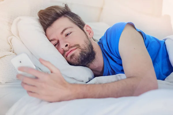 Nada mejor que despertar a ese texto especial. Recortado disparo de un joven guapo mensajes de texto en su teléfono móvil mientras yacía en la cama en casa. — Foto de Stock