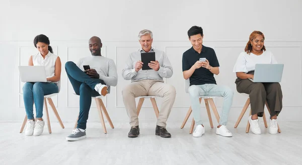 Göra några värdefulla kontakter medan de väntar. Skjuten av en skiftande grupp människor som använder digitala enheter medan de sitter i kö mot en vit bakgrund. — Stockfoto