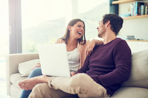 Compartir una risa en línea. Foto de una joven pareja sonriente usando un portátil mientras se relaja en el sofá en casa. — Foto de Stock