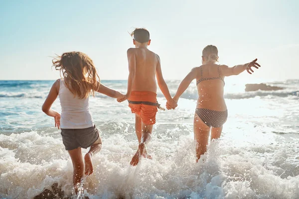 Jsme připraveni se namočit. Postřelen sourozenci běží do vody na pláži za slunečného dne. — Stock fotografie