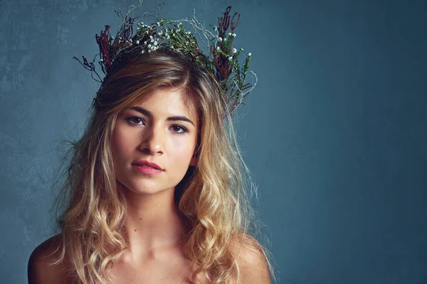 Organic beauty. Cropped shot of a young woman posing with flowers in her hair against a blue background. — Stock Photo, Image