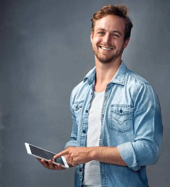 Manter as coisas sociais online. Retrato de um jovem bonito usando um tablet contra um fundo cinza no estúdio. — Fotografia de Stock