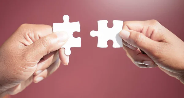 Résoudre le puzzle, pièce par pièce. Plan recadré de deux hommes d'affaires méconnaissables ajustant des pièces de puzzle ensemble en studio sur un fond rouge. — Photo