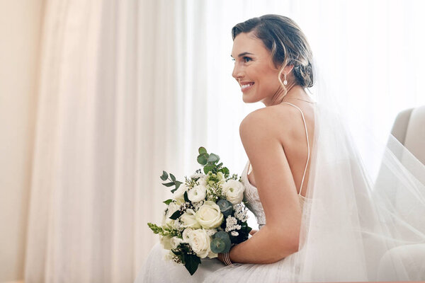 Radiantly beautiful on her wedding day. Cropped shot of an attractive young bride sitting alone in the dressing room and holding her bouquet of flowers.