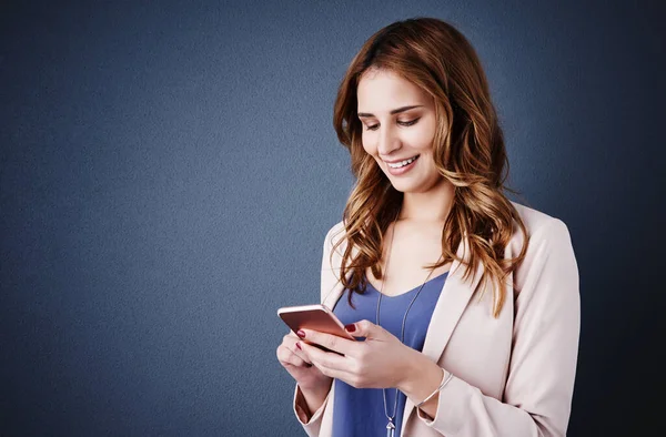 La forma más rápida de comunicarse con los clientes. Captura de estudio de una atractiva joven empresaria usando un teléfono móvil sobre un fondo azul oscuro. —  Fotos de Stock