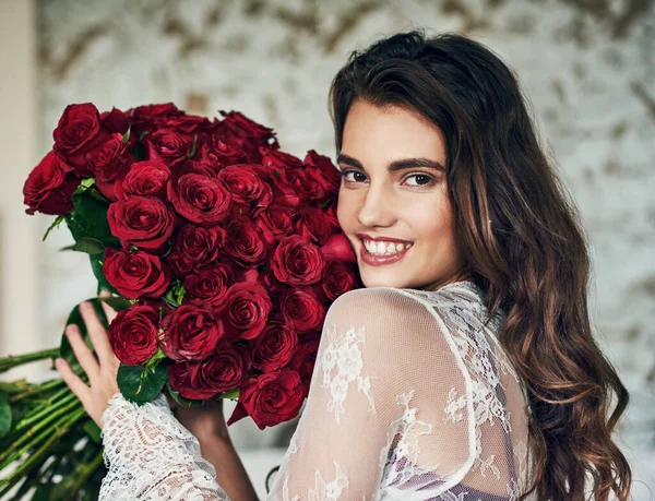 A rózsák pirosak, ahogy az ajkai is. Portré egy gyönyörű fiatal nőről, aki az ágyán pihen, miközben egy csokor rózsát tart a kezében.. — Stock Fotó