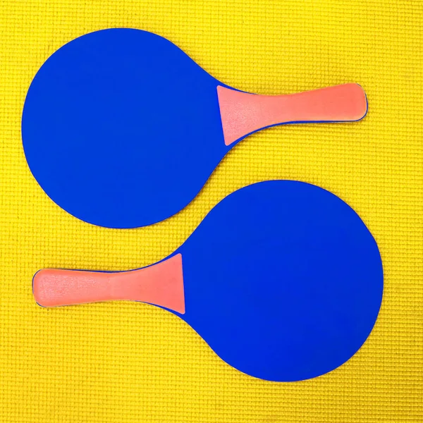 Ci vogliono due per il tango. Colpo ad angolo alto di due racchette da ping pong blu poste sopra uno sfondo giallo all'interno di uno studio. — Foto Stock