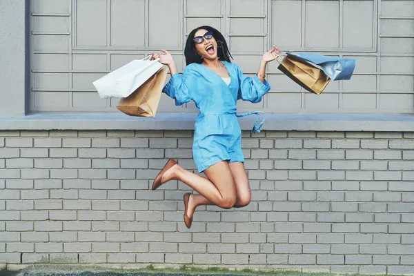 Compras faz com que cada menina pule de alegria. Tiro de comprimento total de uma jovem mulher atraente pulando de alegria enquanto segurando sacos de compras contra uma parede de tijolo. — Fotografia de Stock