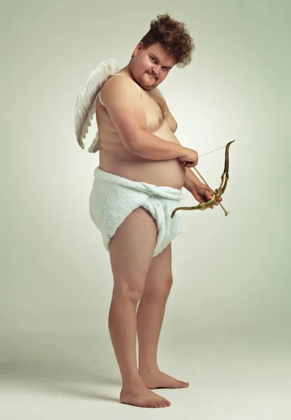 Shooting straight. An obese man dressed as a cherub with a bow and arrow. — Stock Photo, Image