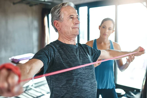 Підтримка здорових м'язів незалежно від віку. Знімок старшого чоловіка за допомогою опірних смуг за допомогою фізичного терапевта . — стокове фото