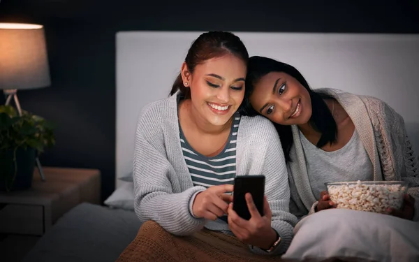 Sollte ich diese herunterladen? Aufnahme einer jungen Frau, die ihrem Freund etwas auf ihrem Handy zeigt, während sie zusammen auf einem Bett sitzt. — Stockfoto