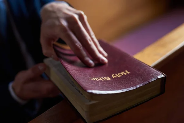 Encontrar conforto no bom livro. Tiro cortado de um homem que abre uma bíblia enquanto está sentado em um banco na igreja. — Fotografia de Stock