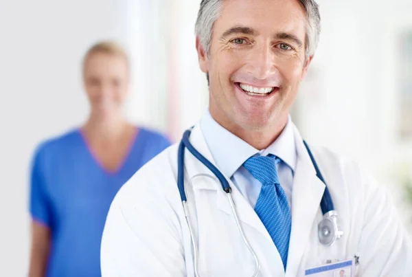 Våra patienters hälsa är det enda viktiga. Porträtt av en manlig läkare med en kollega stående i bakgrunden. — Stockfoto
