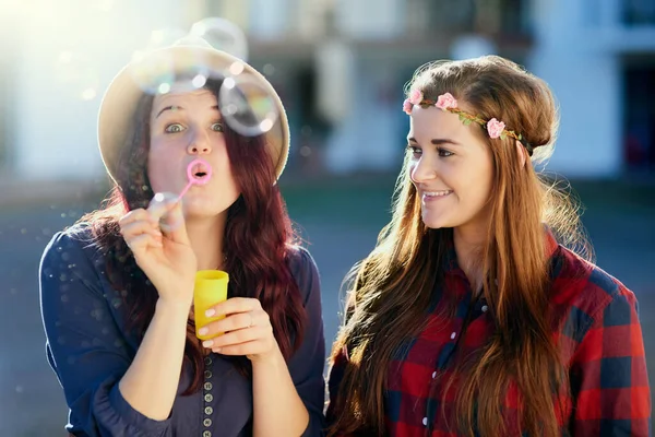 Be less serious and more silly instead. Shot of two young friends blowing bubbles outside. — Stock Photo, Image