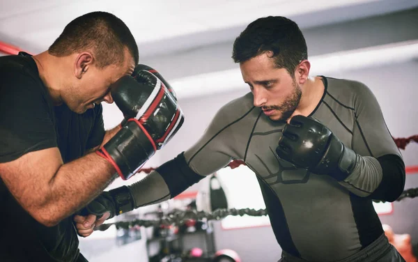 Mãos para cima. Tiro de dois jovens boxers masculinos enfrentando um ao outro em um jogo de treino dentro de um ringue de boxe em um ginásio durante o dia. — Fotografia de Stock