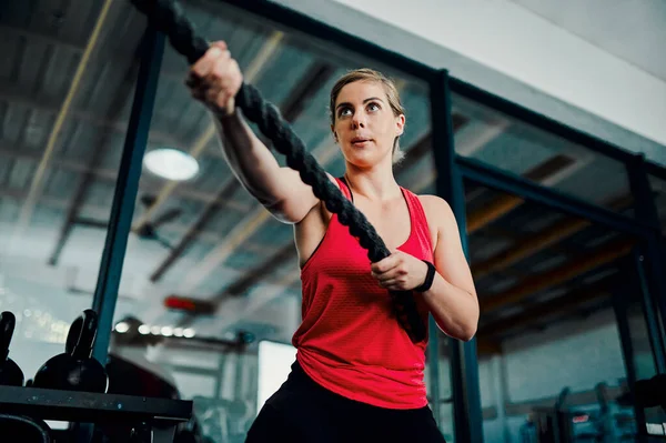 Bitva pokračuje. Vystřižený záběr atraktivní mladé atletky cvičit s bojovými provazy v tělocvičně. — Stock fotografie
