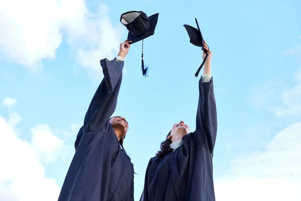 Sometimes youve just gotta take your hat off. Low angle shot of two attractive young female students celebrating on graduation day. — ストック写真