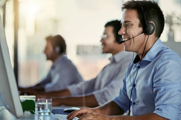 Toegewijd aan de kwaliteit van de klantenservice. Opname van een call center agent die in een kantoor werkt met zijn collega 's op de achtergrond. — Stockfoto