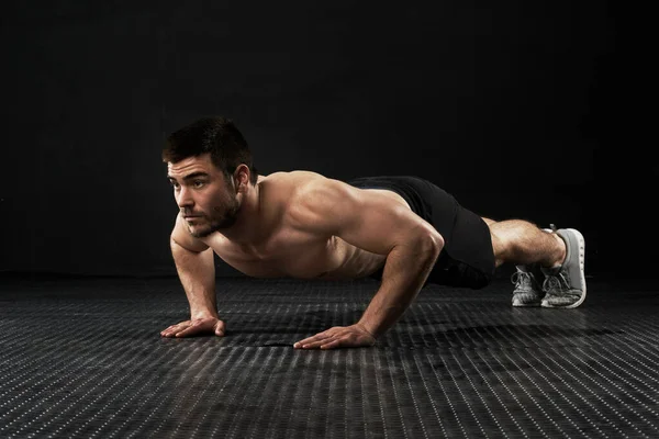 El esfuerzo es solo esfuerzo cuando comienza a doler. Estudio de un joven deportivo haciendo flexiones aisladas en negro. — Foto de Stock