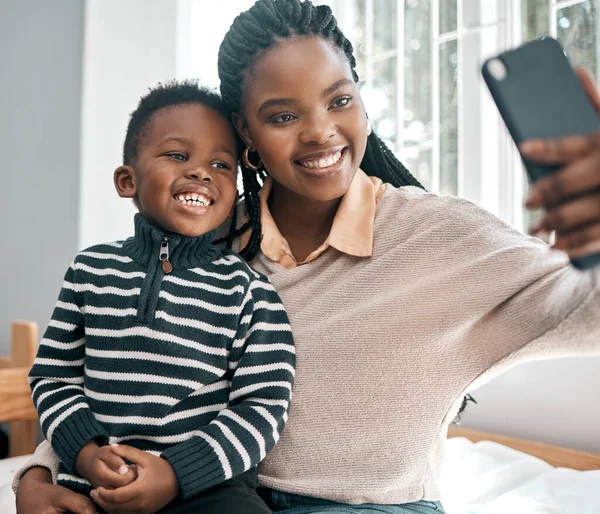 Lächeln. Schnappschuss einer attraktiven jungen Frau und ihres entzückenden Sohnes, die Selfies machen, während sie zu Hause auf einem Bett sitzen. — Stockfoto
