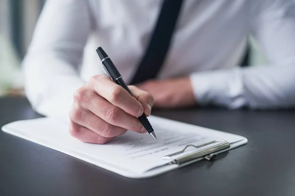 Ik tik alle juiste dozen. Gehakte foto van een zakenman die papierwerk invult op een klembord terwijl hij aan een tafel in een kantoor zit. — Stockfoto