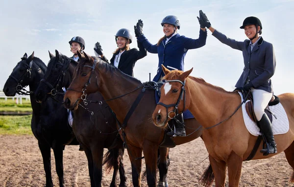 Conseguimos. Tiro cortado de um grupo de atraentes jovens jóqueis do sexo feminino de alta cinco enquanto sentados em seus cavalos costas. — Fotografia de Stock