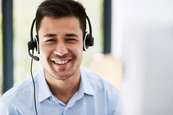 Representing the company brand with positivity and professionalism. Portrait of a happy young man wearing a headset and using a computer at work. — Stock Photo, Image