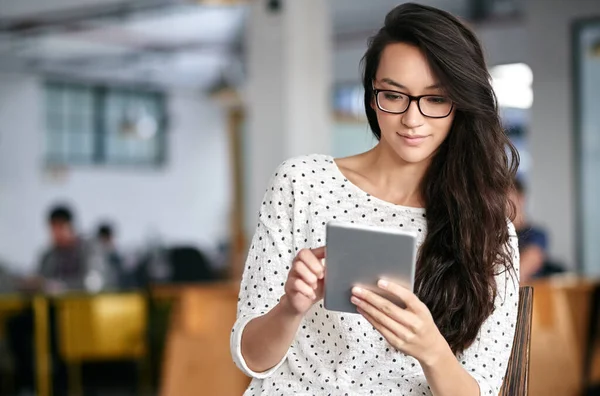 Yhteydessä koko työpäivän. Kuvattu nuori nainen käyttää digitaalista tablettia istuessaan modernissa toimistossa. — kuvapankkivalokuva