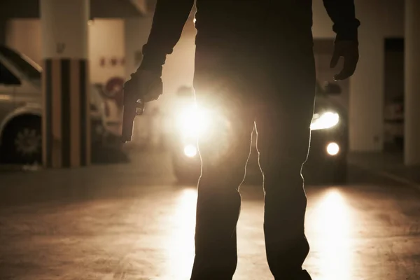 Schatten der Angst. Ein Krimineller hält einen Revolver in der Hand, um jemanden in einer Tiefgarage zu entführen. — Stockfoto