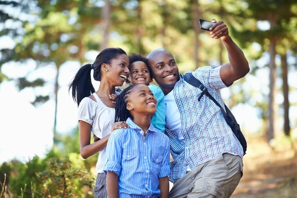 Alla ler och säger naturen. Skjuten av en lycklig familj som tar ett självporträtt med en kamera telefon medan ute vandring i skogen. — Stockfoto