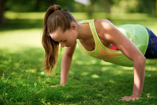 Dedica-te. Tiro de uma jovem mulher fazendo flexões em um campo gramado. — Fotografia de Stock