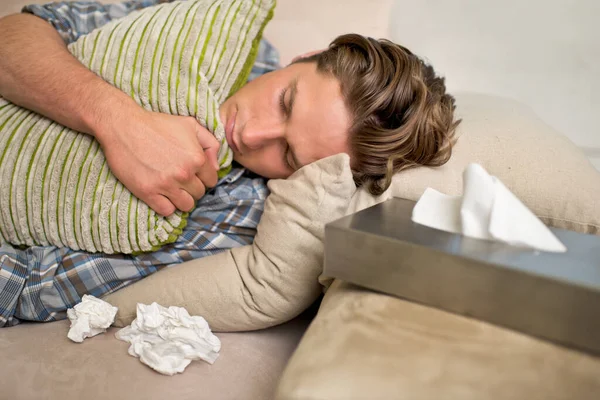 Im sick. I need someone to comfort me.... Shot of a sick young man lying on the sofa with tissues. — Stock Photo, Image