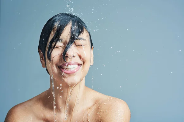 Réveillez-vous à la sensation rafraîchissante de l'eau. Prise de vue d'une jeune femme prenant une douche rafraîchissante sur fond bleu. — Photo