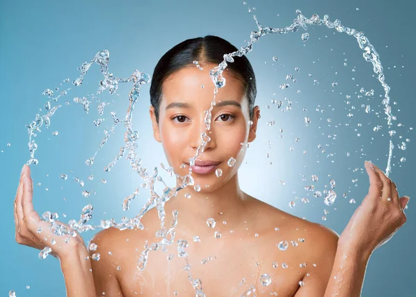 Alle diese Verunreinigungen abwaschen. Aufnahme einer attraktiven jungen Frau, die vor blauem Hintergrund im Studio posiert und ihr Gesicht mit Wasser bespritzt. — Stockfoto