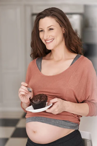 Zwangerschapsverlangens. Gehakt schot van een jonge zwangere vrouw eten van een cupcake in de keuken. — Stockfoto