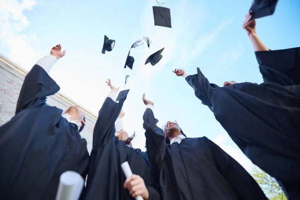 Au prochain chapitre de notre vie. Plan en angle bas d'un groupe d'étudiants jetant leurs casquettes en l'air le jour de la remise des diplômes. — Photo