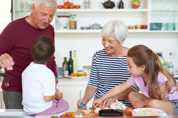 Lunch with the grandparents. Shot of grandparents preparing dinner with their grandchildren in a kitchen. — Stock Photo, Image