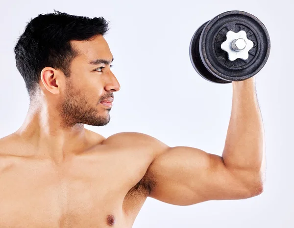 Use high quality equipment. Shot of a young man flexing his bicep muscles while holding a weight against a studio background. — ストック写真