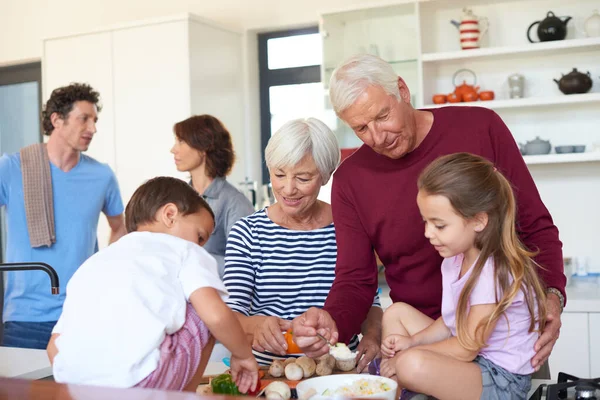 La comida está en el corazón de esta familia. Foto de abuelos preparando la cena con sus nietos en una cocina. —  Fotos de Stock