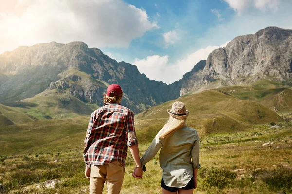 Llegar a nuevas alturas como pareja. Vista trasera de una joven pareja admirando una vista montañosa en la naturaleza. — Foto de Stock