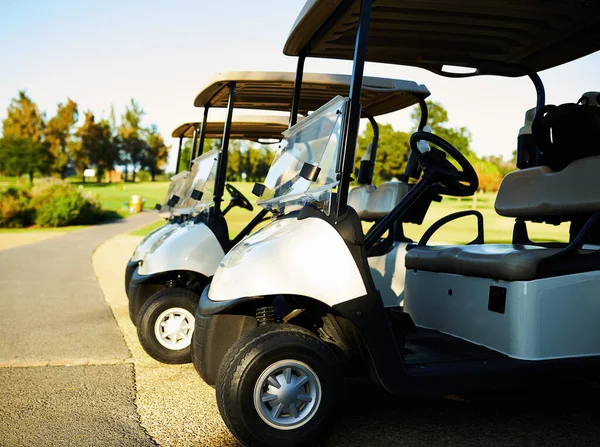 É um bom dia para um jogo de golfe. Tiro de três carrinhos de golfe lado a lado ao lado de um campo de golfe. — Fotografia de Stock