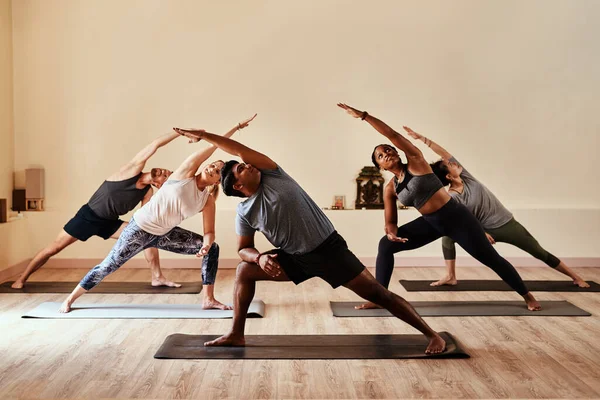 Yoga deixa seu guerreiro interior solto. Tiro de um grupo de jovens homens e mulheres praticando ioga em uma aula de fitness. — Fotografia de Stock