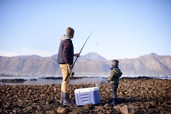 Vamos a tirarlo a la profundidad. Disparo de un padre y un hijo de pie con sus artes de pesca junto al mar. — Foto de Stock