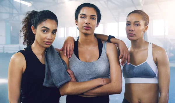 Tillsammans står vi obesegrade. Porträtt av tre unga idrottskvinnor som står och poserar i gymmet. — Stockfoto