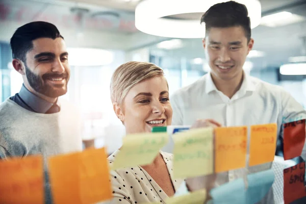 Putting our ideas in a row. Shot of businesspeople brainstorming with sticky notes on a glass wall in the office. — Stock Photo, Image